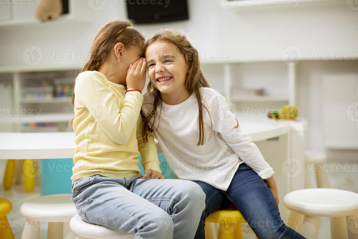 niña susurrando algo al oído de su amiga foto