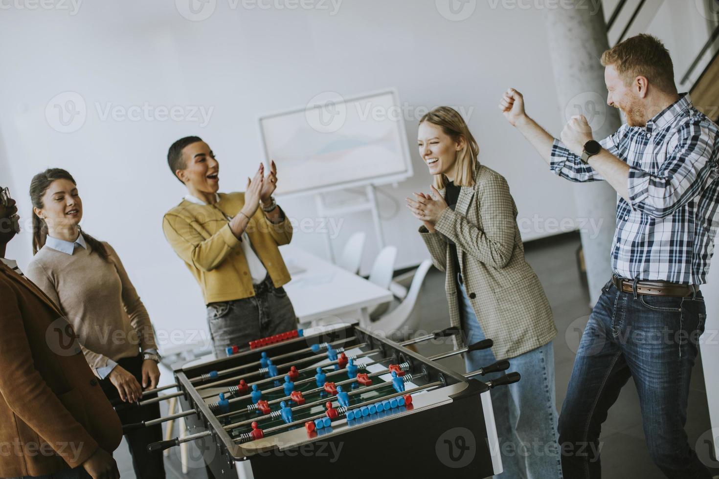 jóvenes empresarios multiétnicos casuales jugando futbolín y relajándose en la oficina foto