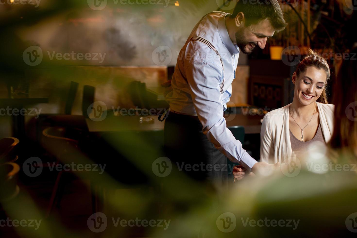 joven mesero sirviendo comida a clientas en el restaurante foto