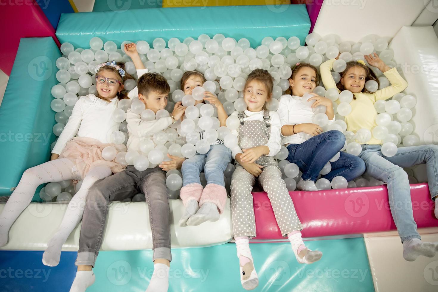 Happy little kids in ball pit smiling happily at camera while having fun photo