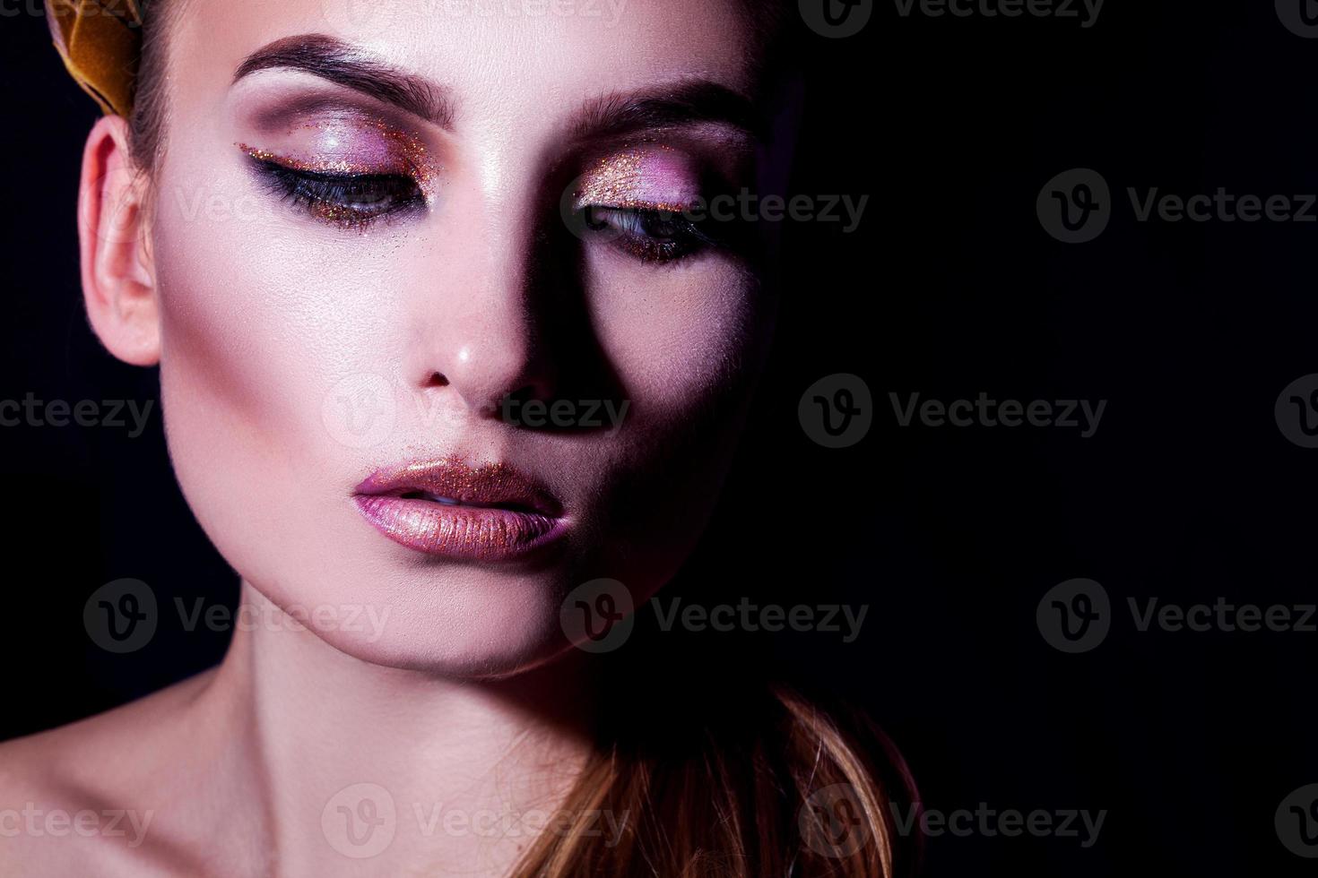 retrato de alto contraste de una hermosa joven adulta con maquillaje y piel sana sobre fondo negro foto