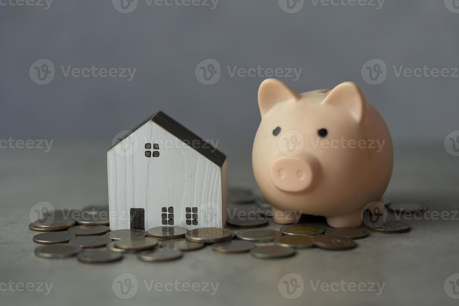 finanzas, casa de madera con hucha rosa y muchas monedas de dinero en el suelo, ahorrar dinero y concepto de bienes raíces. foto