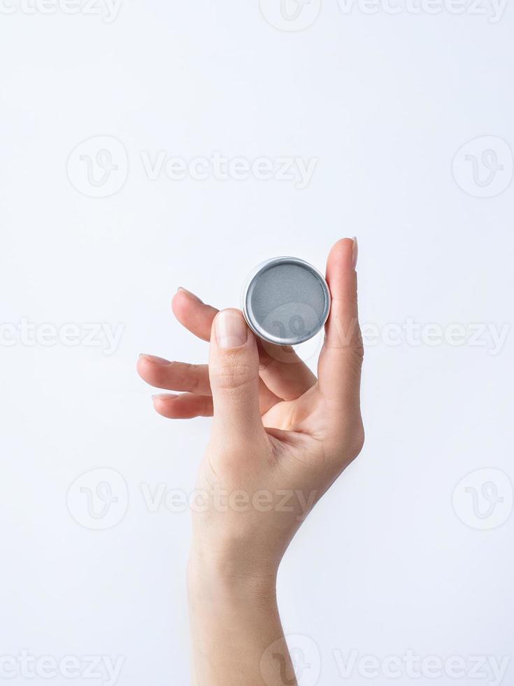 Woman hand holding blank round tin container for lip balm or cream on light gray background photo