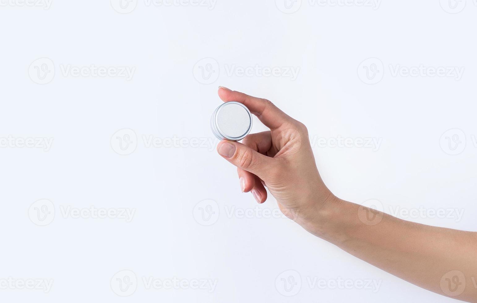 Woman hand holding blank round tin container for lip balm or cream on light gray background photo