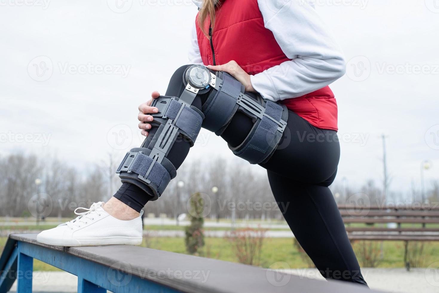 Woman wearing knee brace or orthosis after leg surgery working out in the park photo