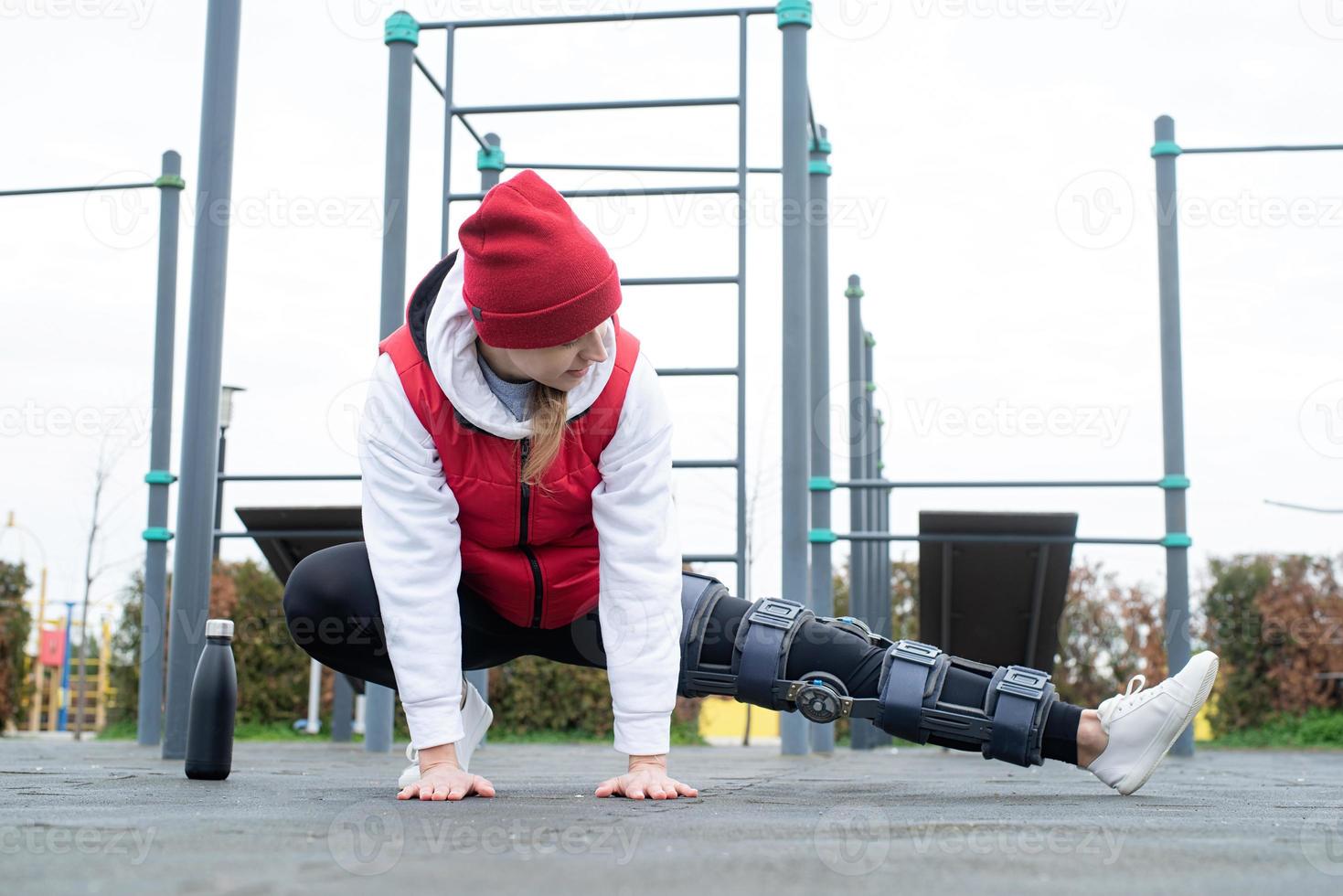 Woman wearing knee brace or orthosis after leg surgery working out in the park photo