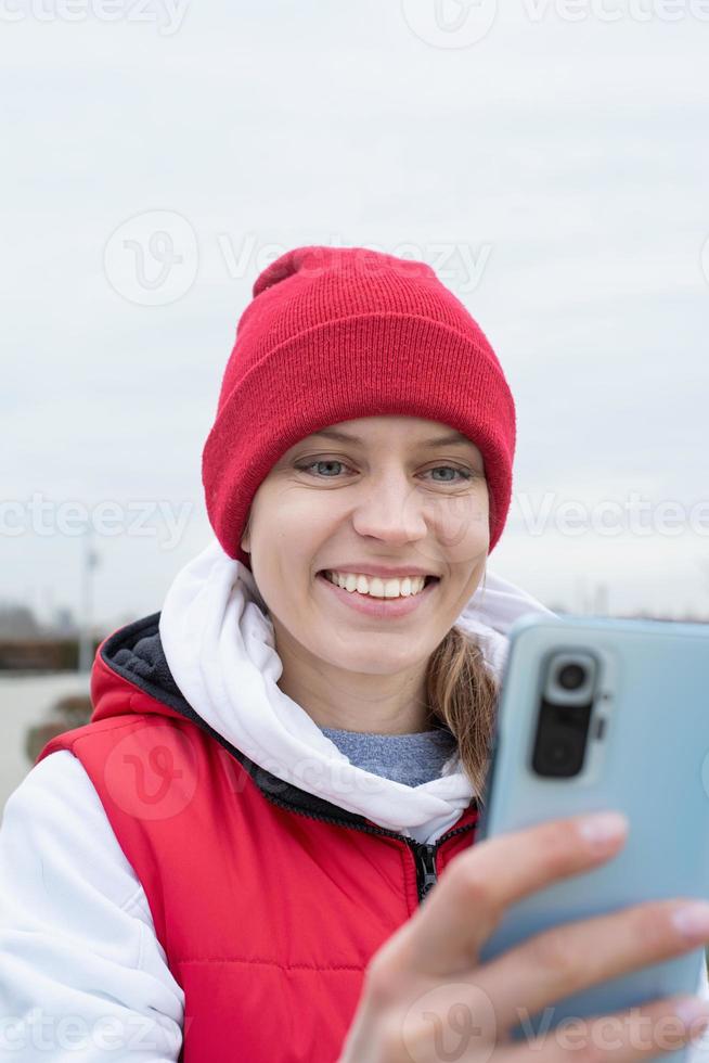 Portrait of young woman in bright red and white warm sport clothes outdoors using smartphone photo