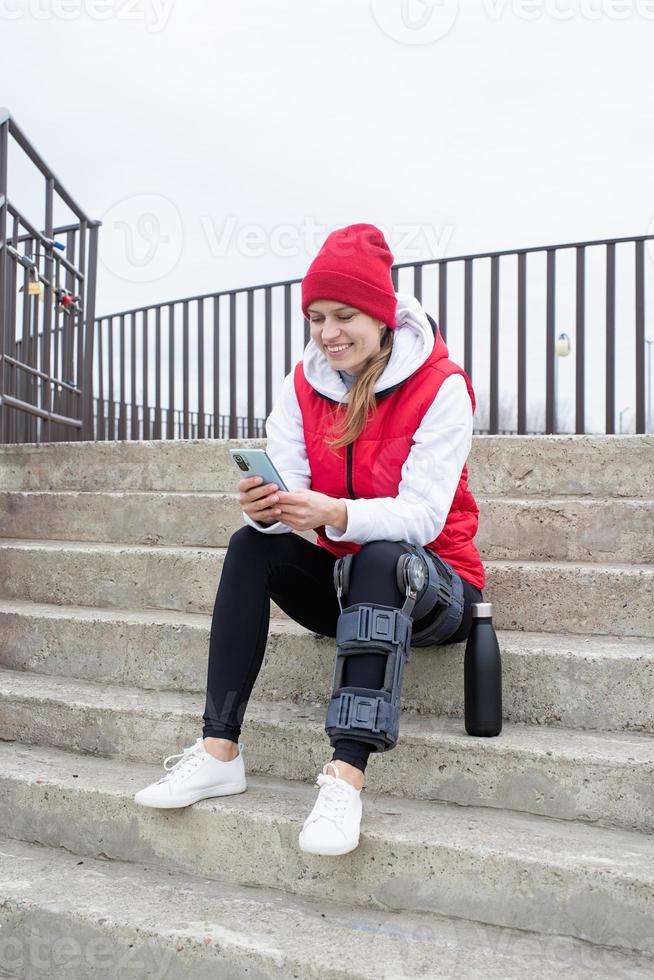 Woman wearing knee brace or orthosis after leg surgery, sitting on stairs ourdoors photo