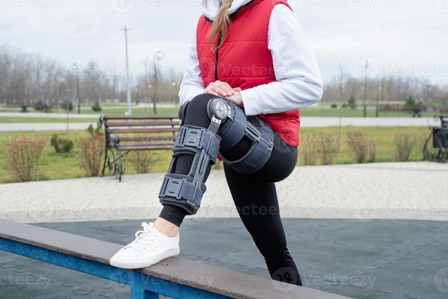 Woman wearing knee brace or orthosis after leg surgery working out in the park photo