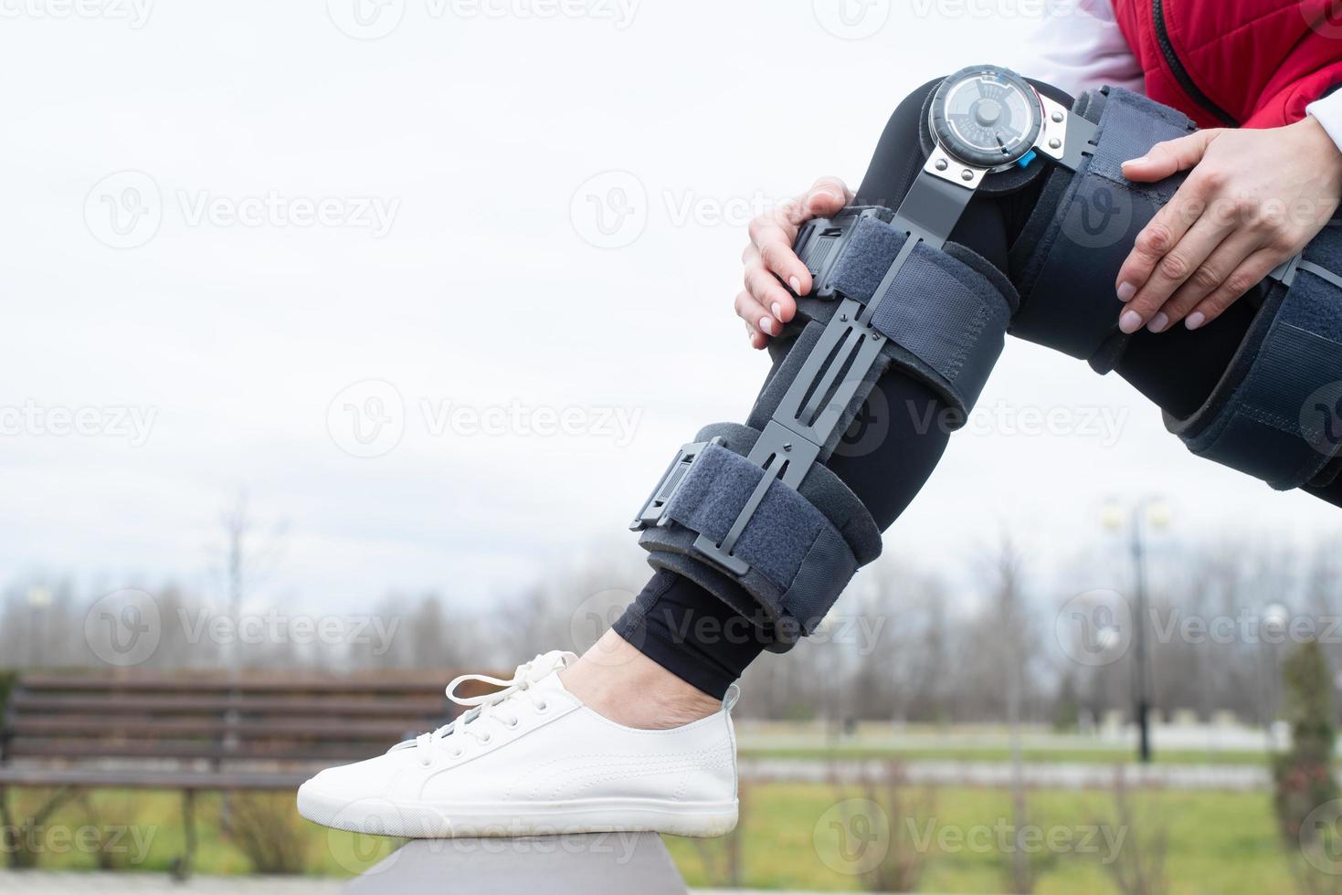 Woman wearing knee brace or orthosis after leg surgery working out in the park photo