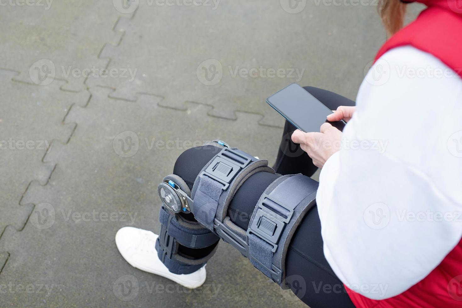 Woman wearing knee brace or orthosis after leg surgery working out in the park photo