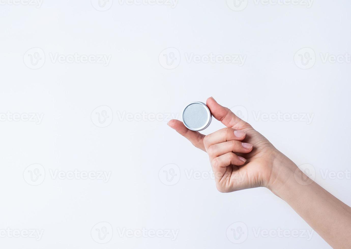 Woman hand holding blank round tin container for lip balm or cream on light gray background photo