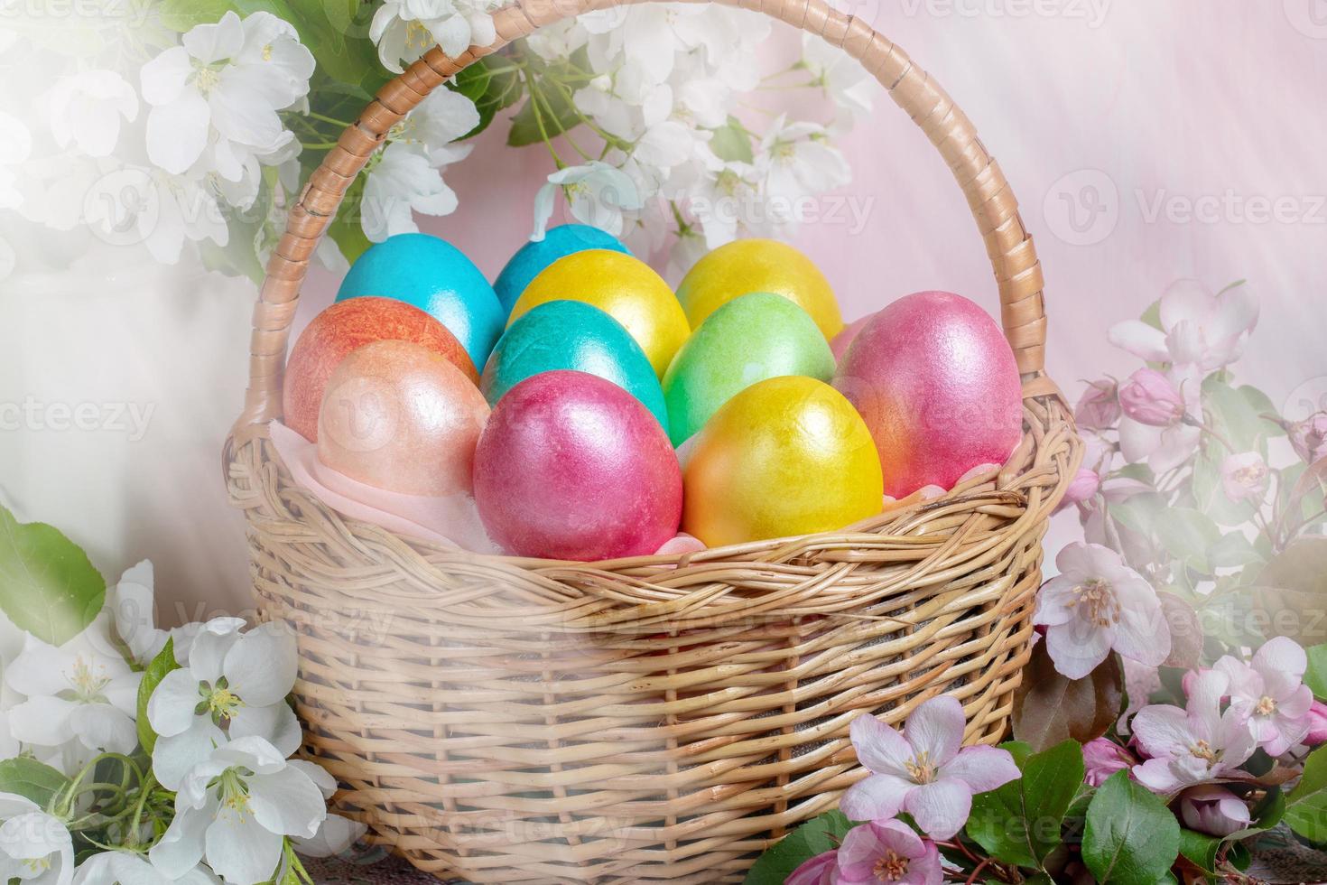 Close-up Easter festive composition of basket of painted Easter eggs and Apple tree twigs on backdrop with light beams. photo