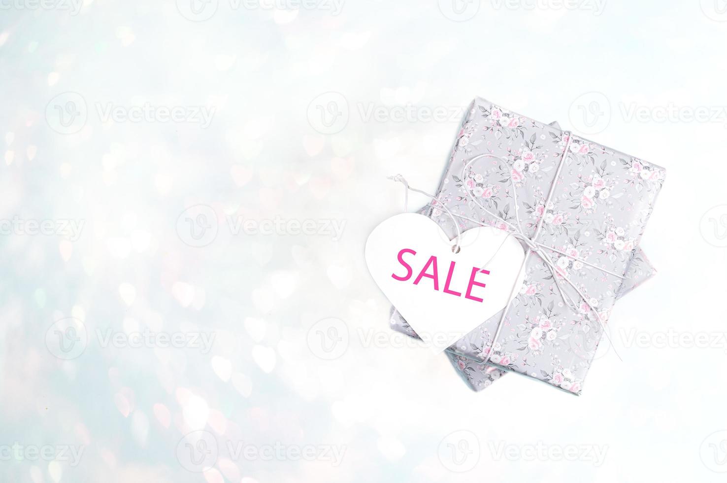 Gift boxes wrapped with grey paper with floral pattern and white heart with word SALE on light blue bokeh backdrop. photo