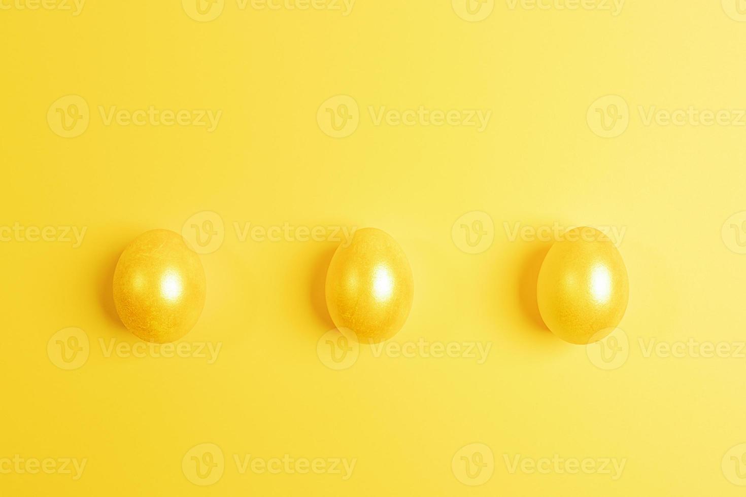 tres huevos de pascua pintados de amarillo brillante yacen en fila sobre fondo amarillo. vista superior. foto