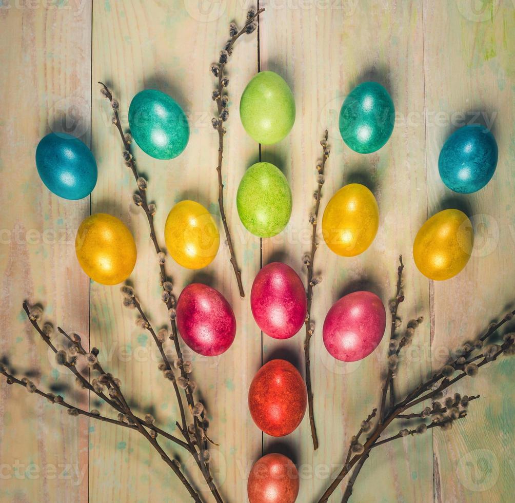 Easter festive layout with soft focus with color Easter eggs, willow twigs on wooden boards. Warm toning. Square photo. photo