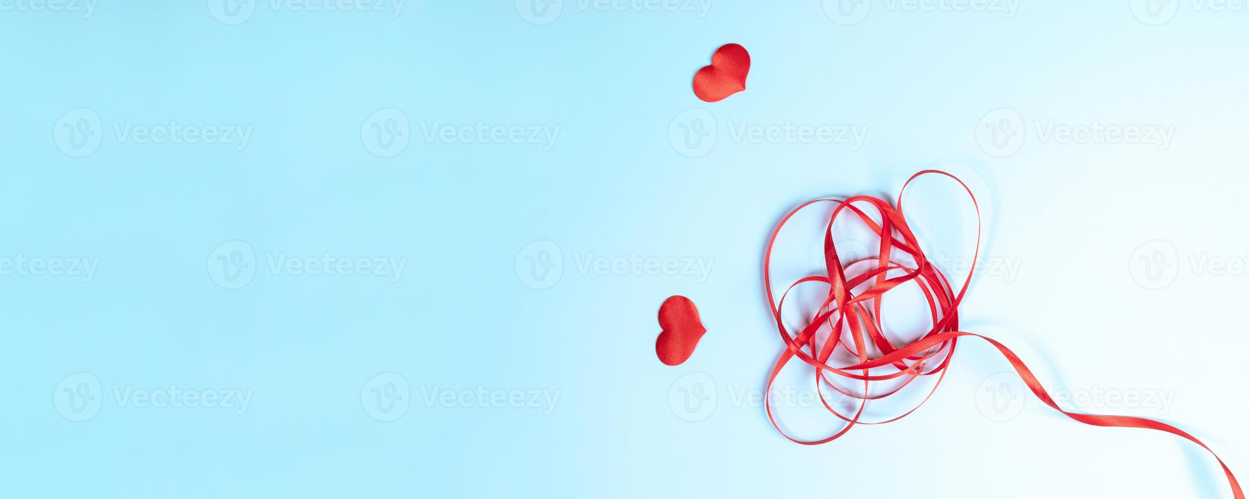 Red ribbon folded as flower and two hearts on light blue background. Valentine's day creative banner. photo