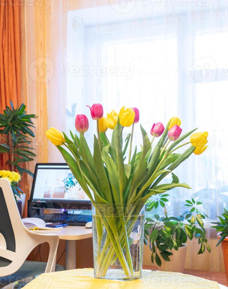 Cozy home holiday 8 March, birthday, Valentine day with tulips vase with home workplace on backdrop. photo