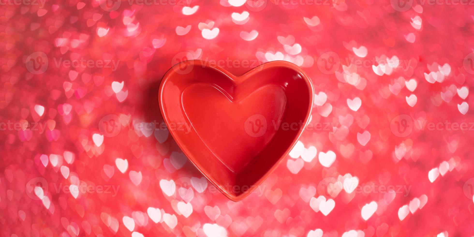 Close-up three red roses in red vase shaped heart on pink bokeh background with hearts. photo