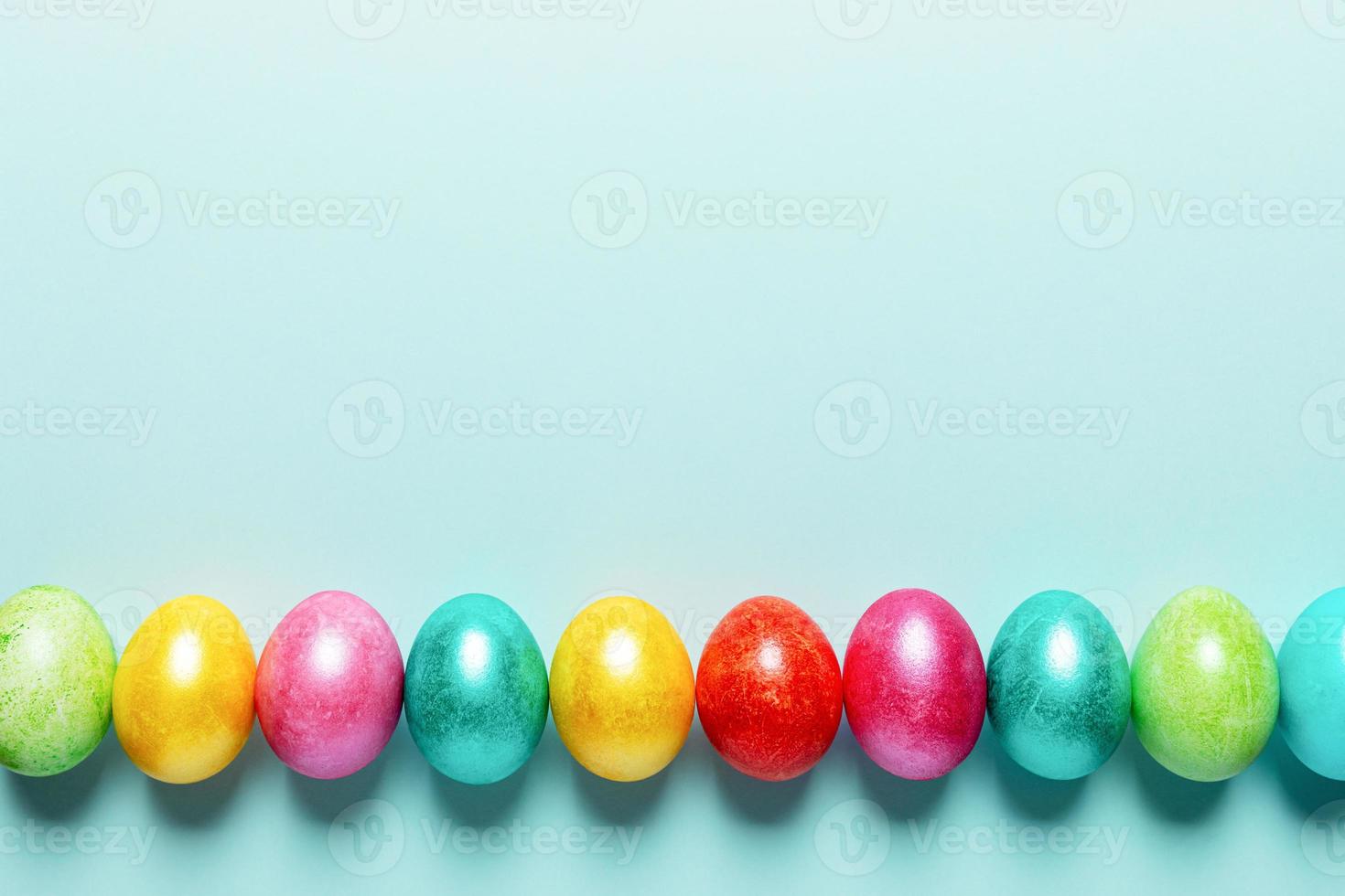 Row of brightly colored Easter eggs with dark shadows on trendy Neo Mint pastel backdrop. Easter festive blank layout. photo