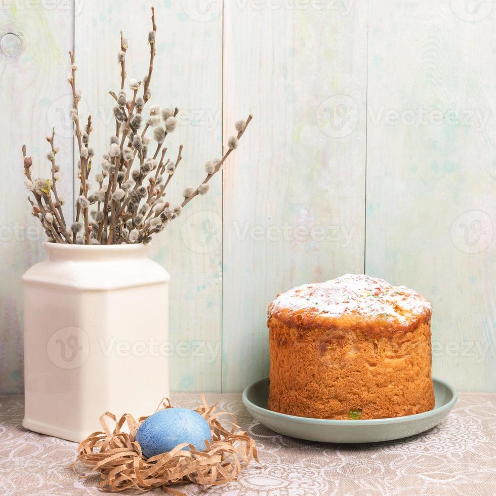 Easter decorations Easter cake, egg in nest and willow branches in vase on light painted wooden wall background. photo