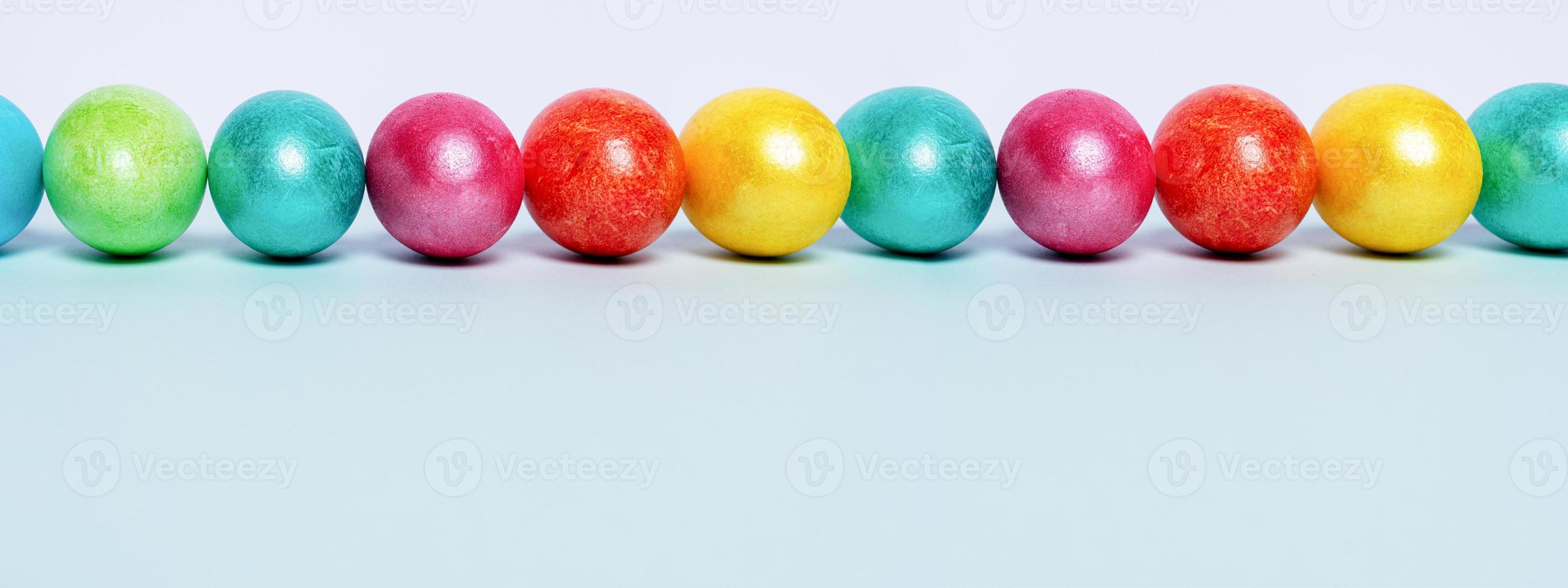 Row of brightlypainted glossy Easter eggs on light blue background. Easter banner. Copy space, low angle. photo