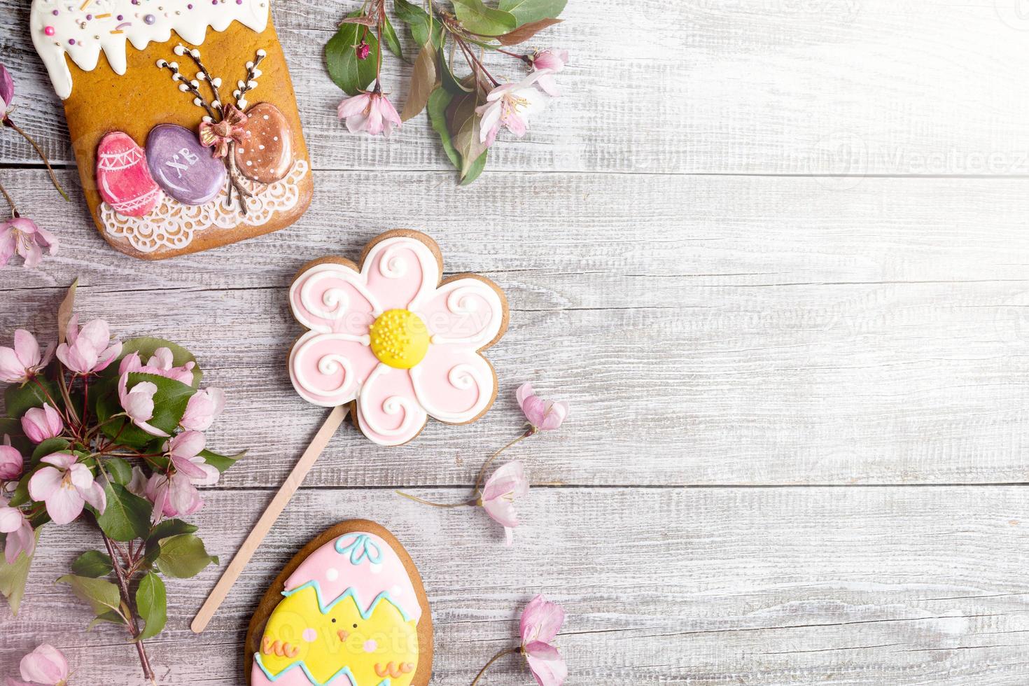 Easter decorations laid out on wooden table. Pink Apple tree branches, gingerbreads as Easter cake, flower and egg. photo