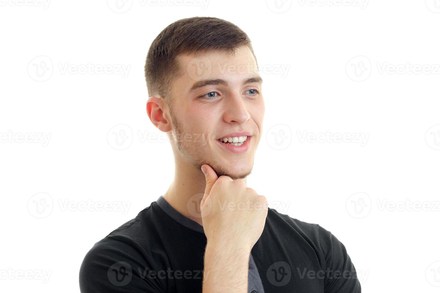 charming young guy is smiling looks away and keeps a hand near the Chin close-up photo