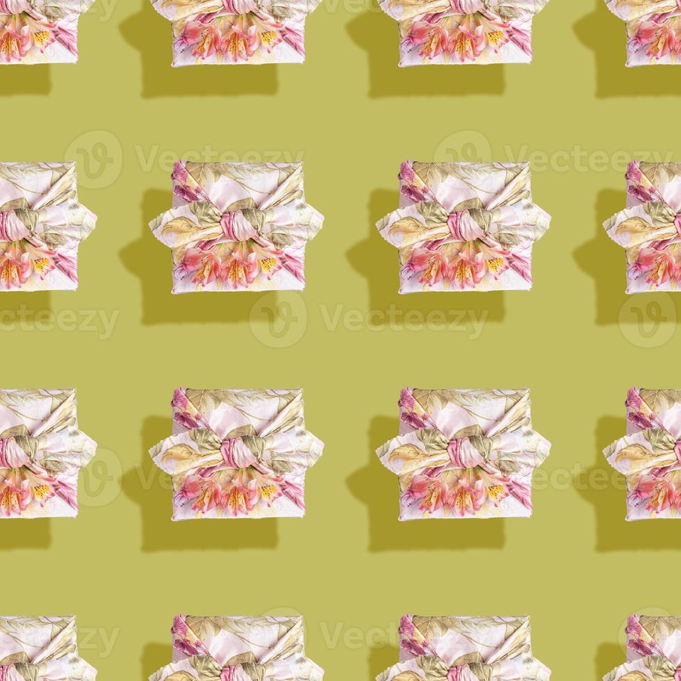Seamless pattern of gift boxes trendy wrapped in cloth in Furoshiki technique with flowers and shadows on green. photo