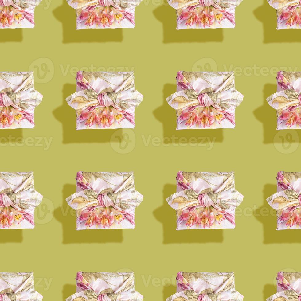 Seamless pattern of gift boxes trendy wrapped in cloth in Furoshiki technique with flowers and shadows on green. photo