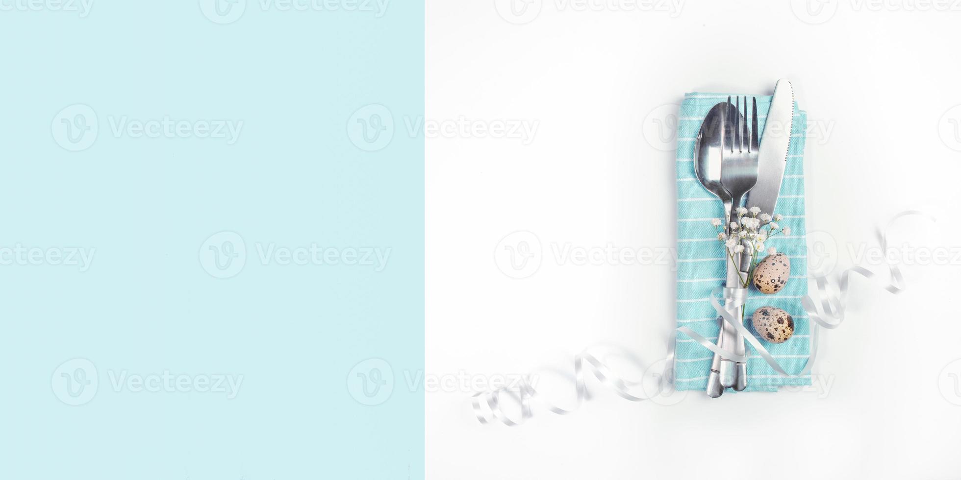 Flatware decorated with white flowers and ribbon and Easter quail eggs on napkin on white and light blue. Copy space. photo