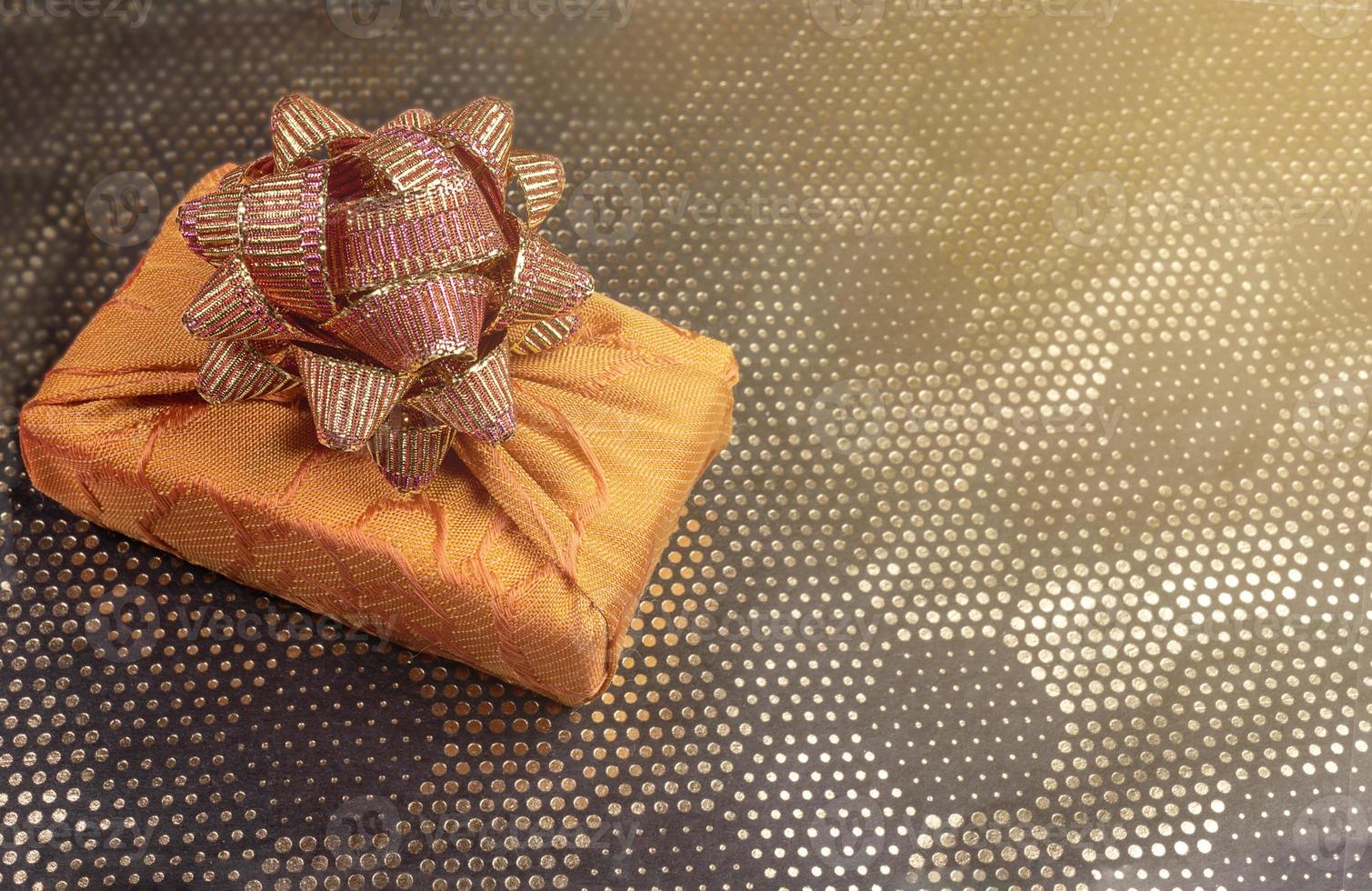 caja de regalo, envuelta en tela amarilla en técnica furoshiki sobre fondo dorado con patrón hexagonal de puntos. copie el espacio foto