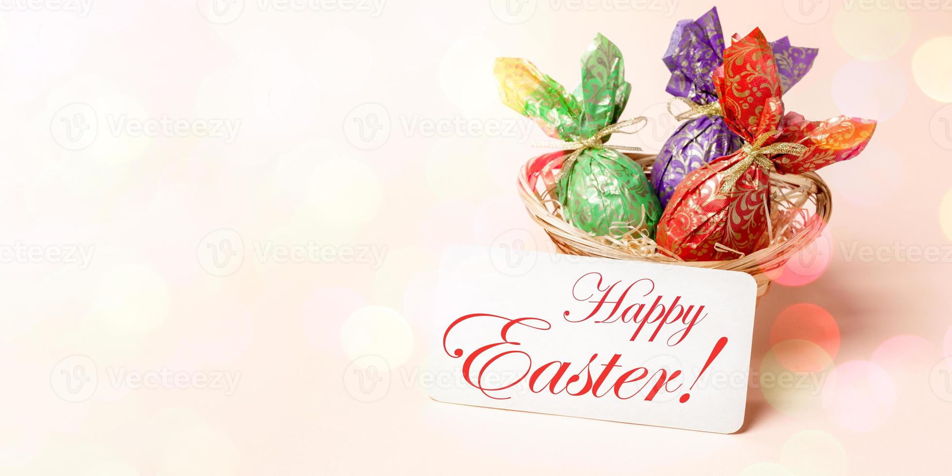 Easter banner. Basket with eggs wrapped in color paper, note Happy Easter on pink with bokeh lights. photo