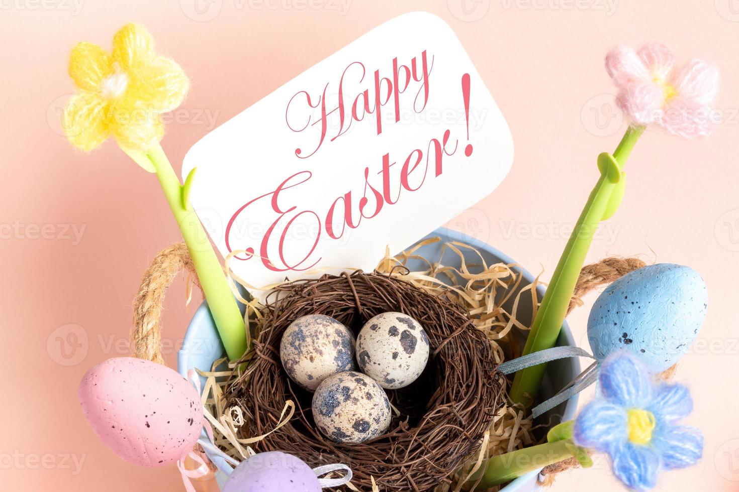 Easter card with nest of quail eggs, decorative eggs, flowers, note Happy Easter close up on pink. photo