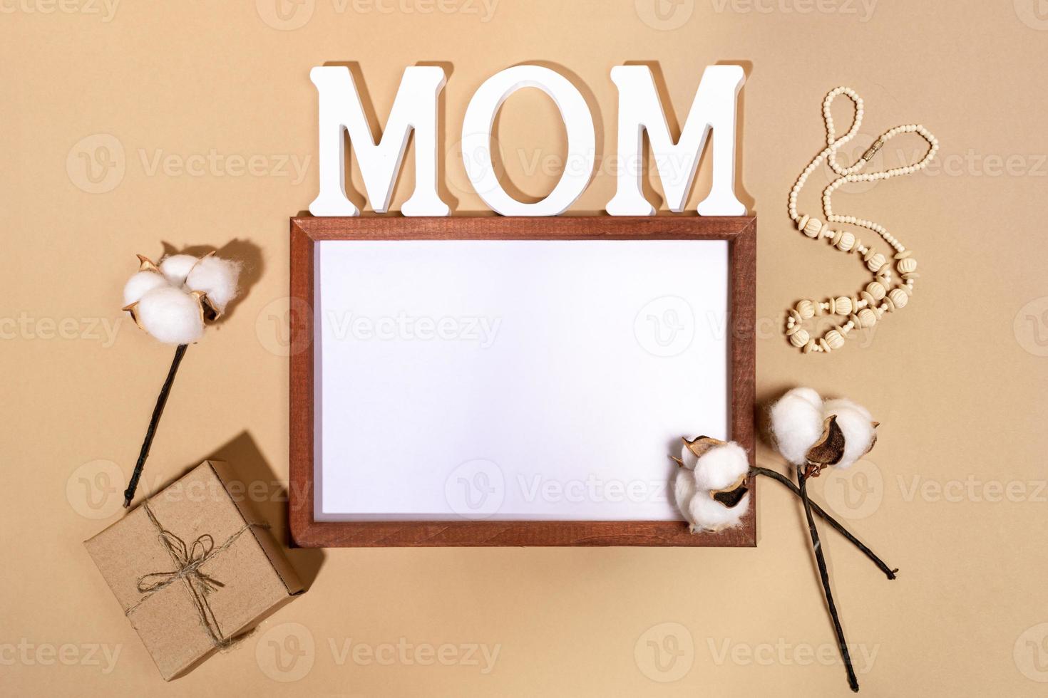 Festive layout for Mother's day with frame, letters MOM, diy gift box and cotton cobs on beige. Mock up. Copy space. photo