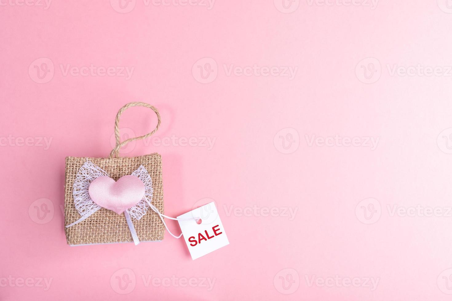 Small decorative wicker handbag and white paper card with words SALE on pink background. Valentine's day sale concept. photo