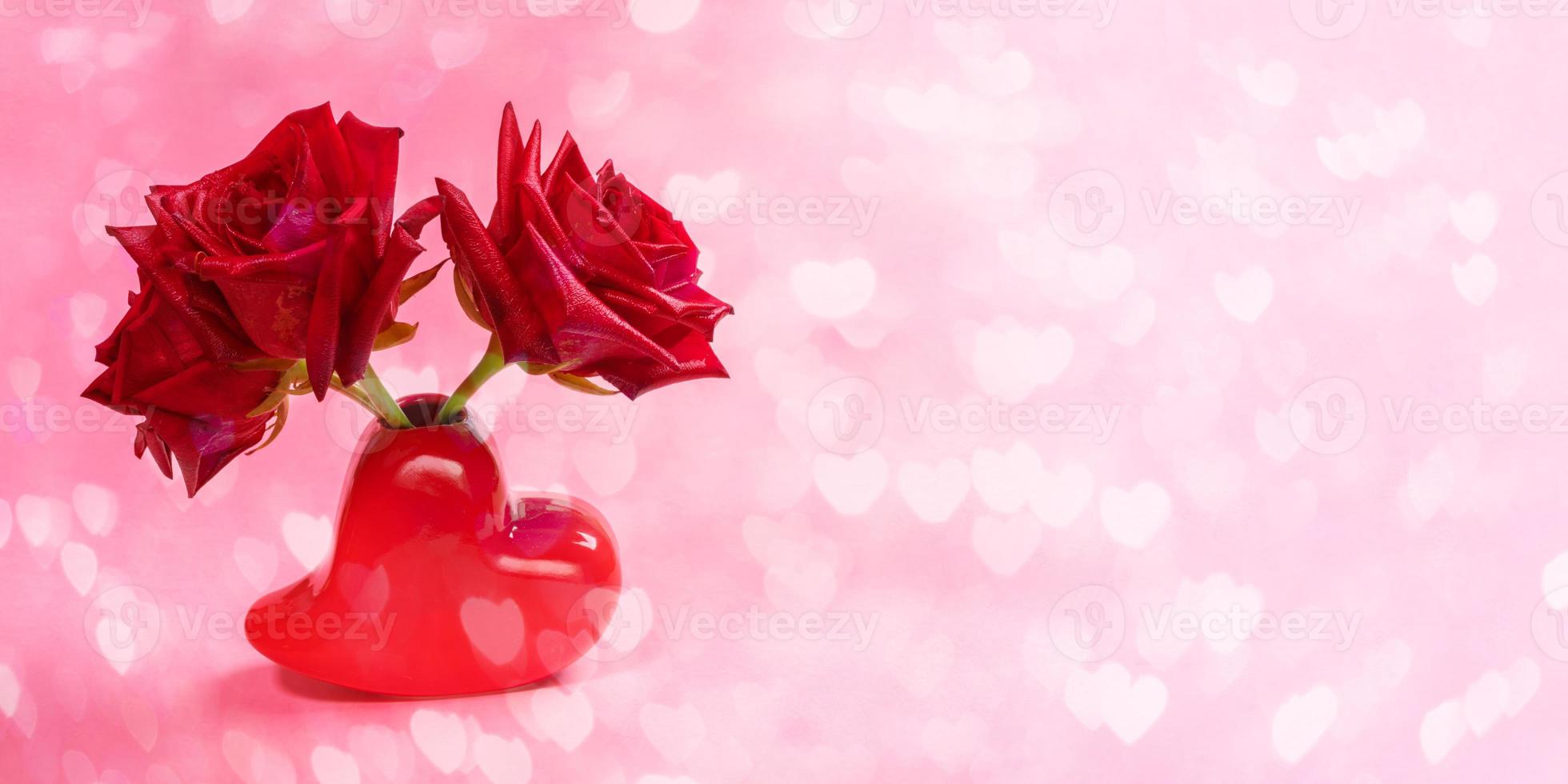 Close-up three red roses in red vase shaped heart on pink bokeh background with hearts. Valentines day or mothers day festive banner. photo