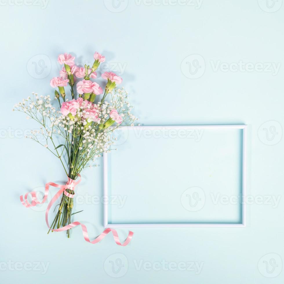 Frame, bouquet of pink carnation and gypsophila flowers with ribbon on light blue. Mother's day. photo