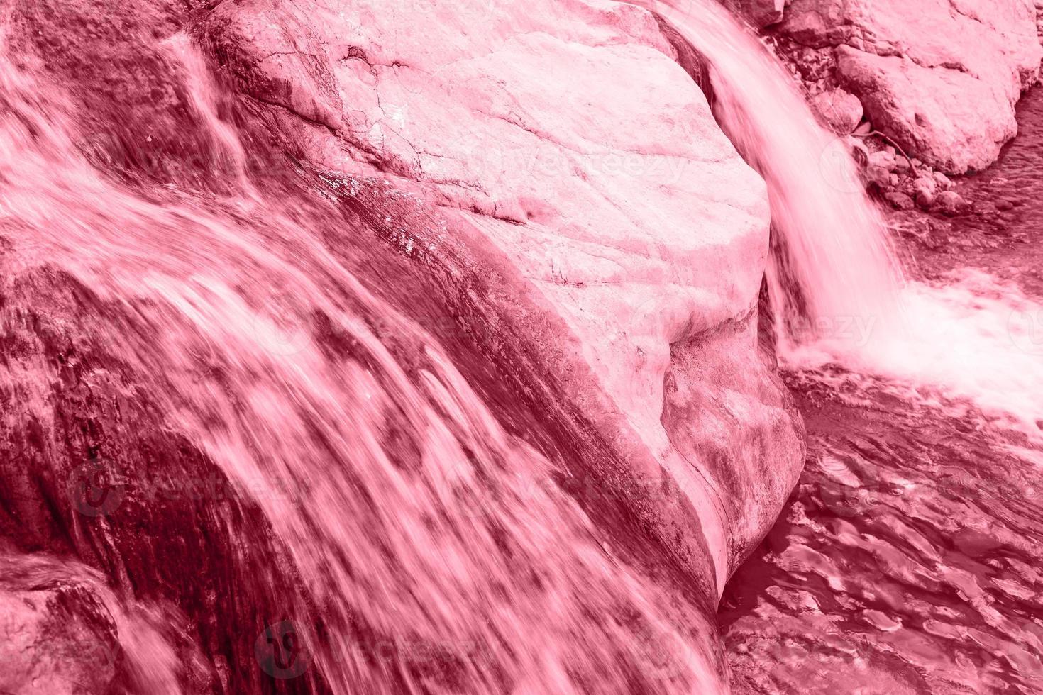 Close up small waterfall on a stone mountain river toned in color 2023 Viva Magenta. photo