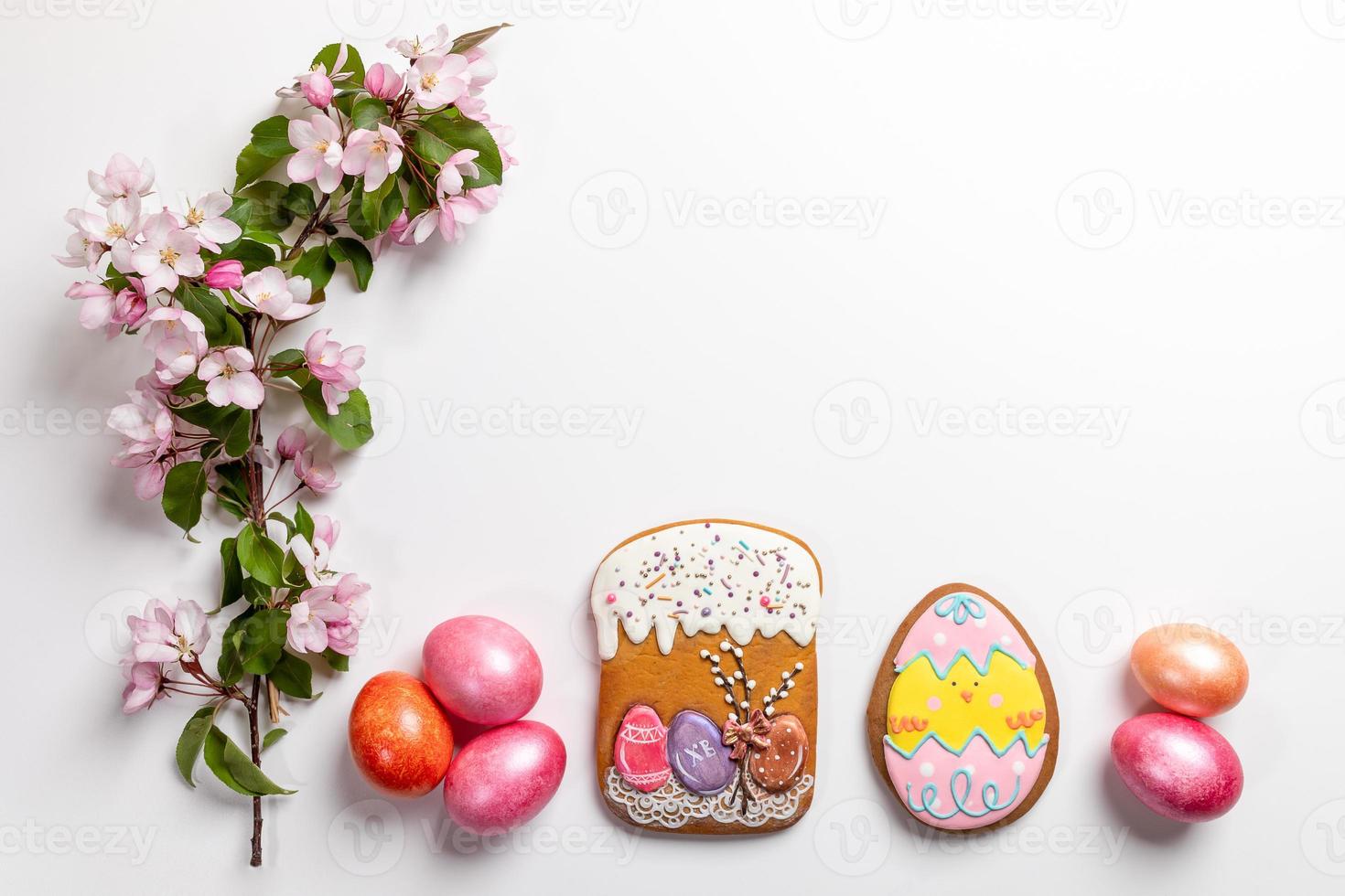 Easter festive arrangement in row of gingerbreads, colored eggs and pink Apple tree twig on white backdrop. Copy space. photo