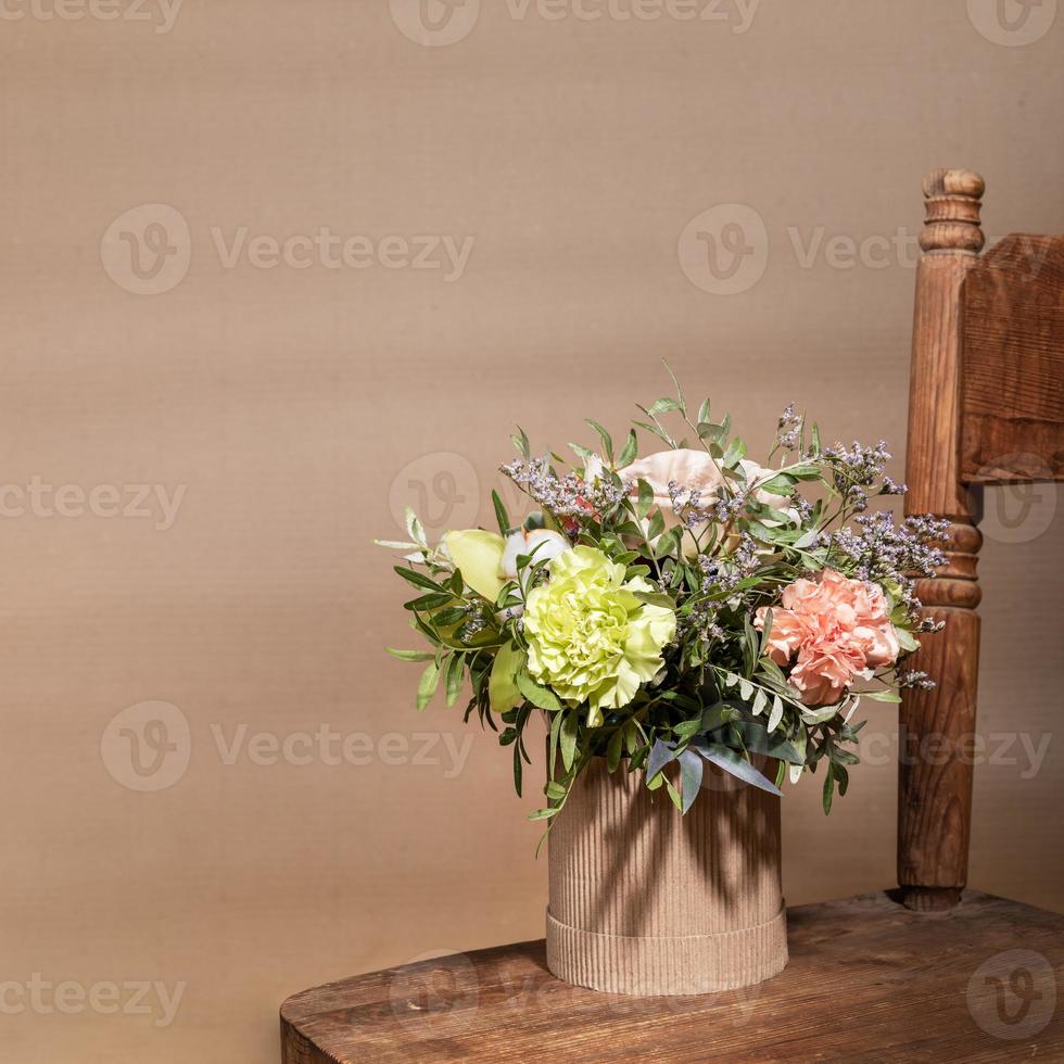 Flowers bouquet in ecological DIY cardboard vase standing on old wooden chair on beige with shadows and copy space. photo