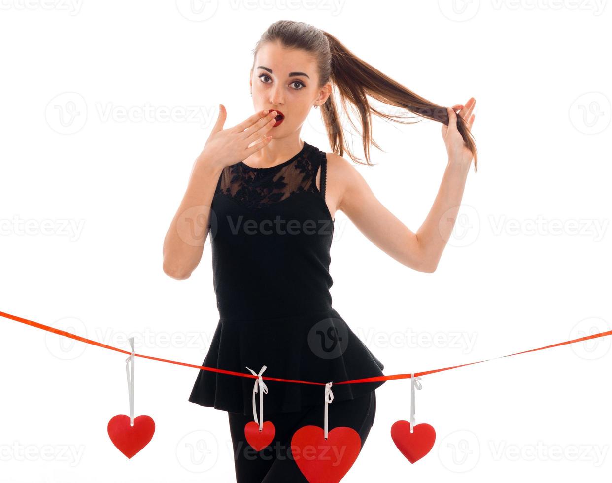 beautiful young girl in a black dress stands near the tape with cards in the shape of hearts and surprise keeps hand near mouth photo