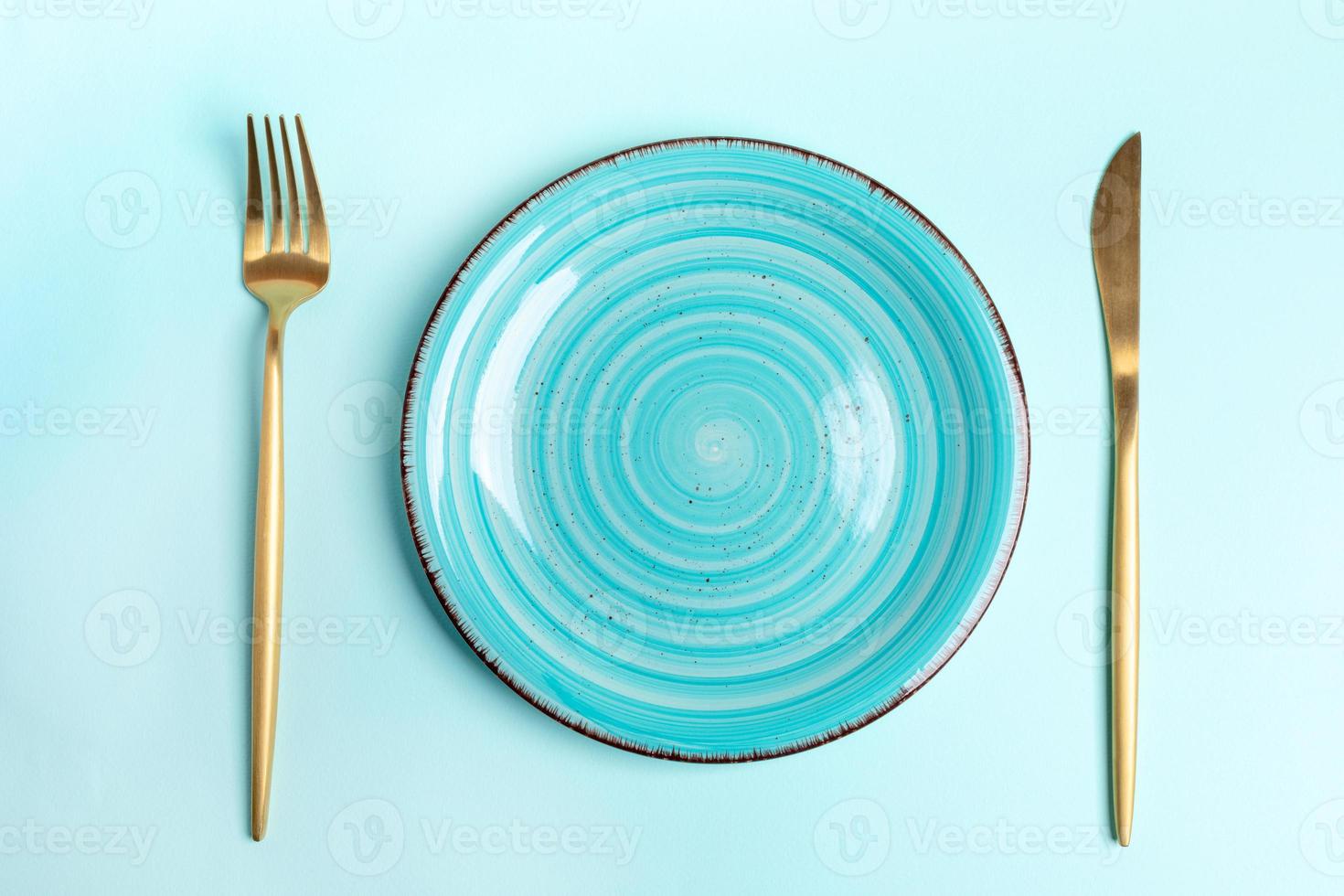 Empty blue round ceramic plate with golden cutlery on light blue backdrop. Top view. photo