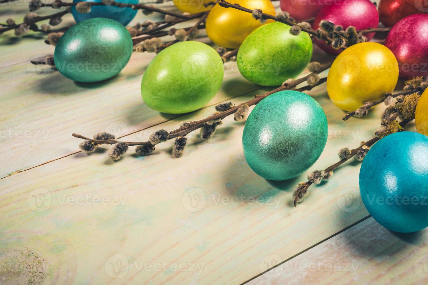 tarjeta de felicitación festiva de pascua con huevos de pascua de colores y ramitas de sauce sobre fondo de madera pintada. enfoque selectivo. foto