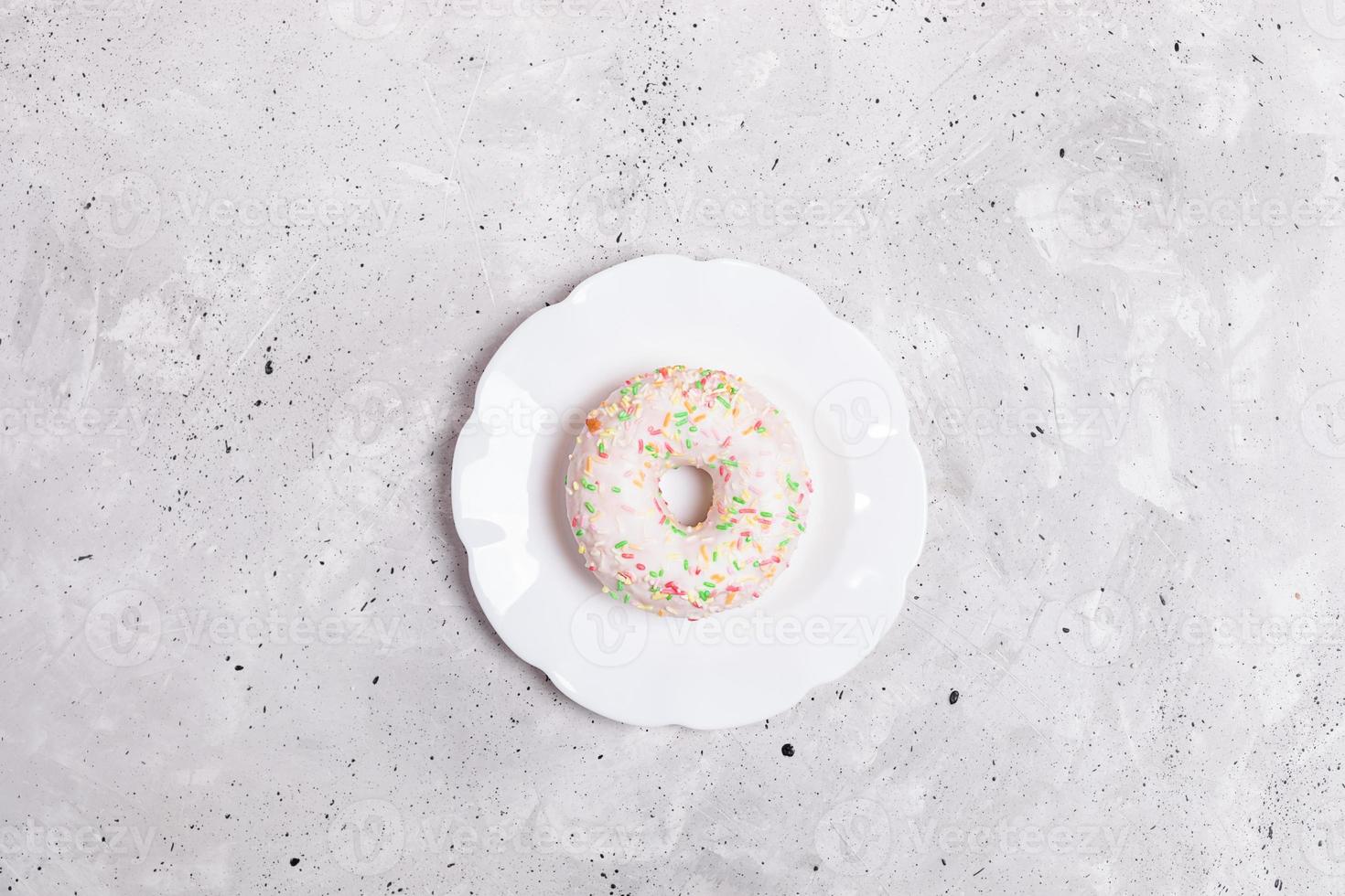 One white glazed doughnut  is lying on white plate in center of grey concrete background. Top view. photo