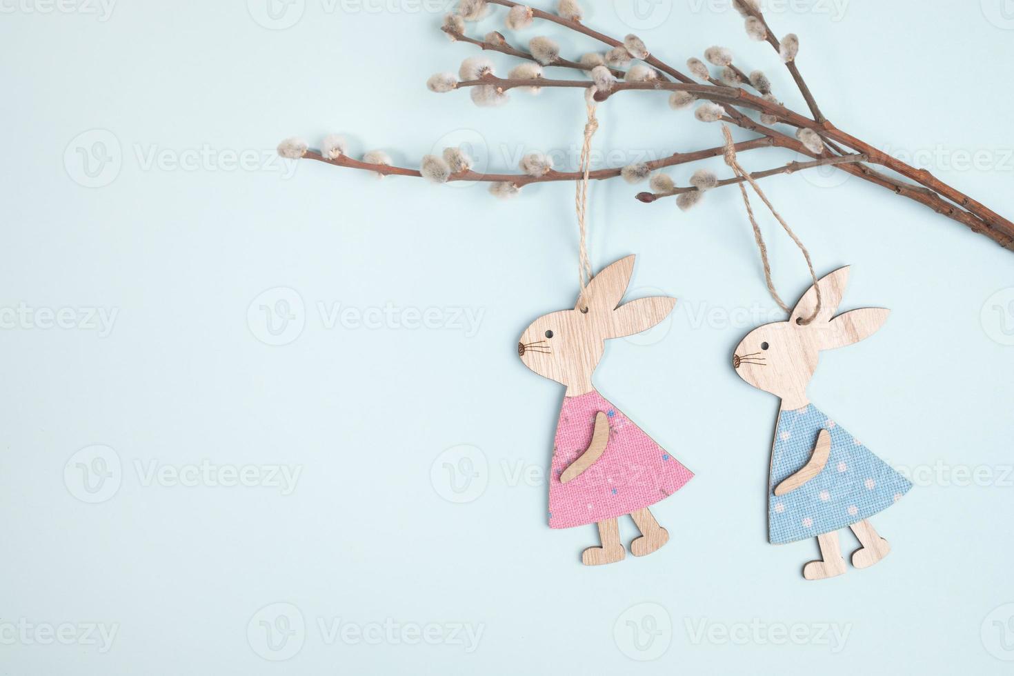 Two funny cute wooden Easter bunnies hanging on willow twigs on pastel light blue background with copy space. photo