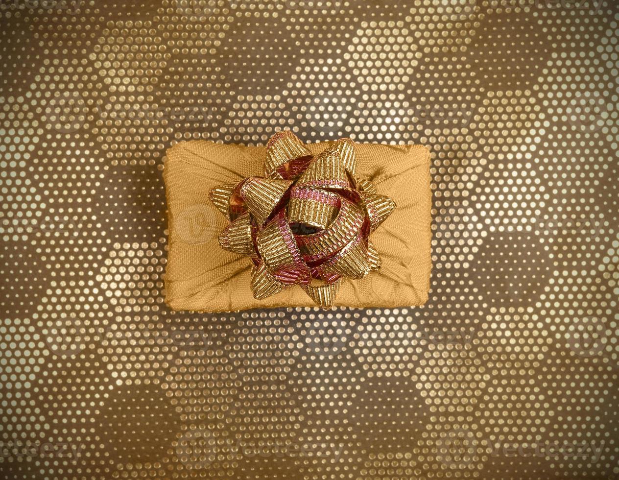 Top view gift box, wrapped in yellow fabric in Furoshiki technique on golden backdrop with dot hexagonal pattern. photo