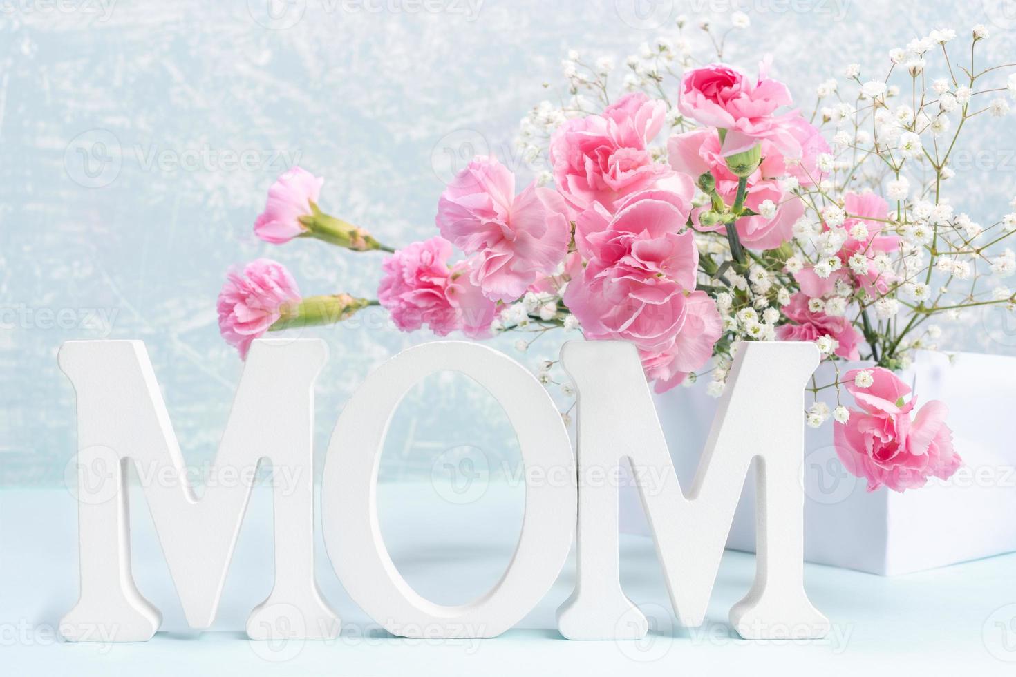 tarjeta del día de la madre con letras blancas mamá, claveles rosas y flores de gypsophila en gris claro. foto