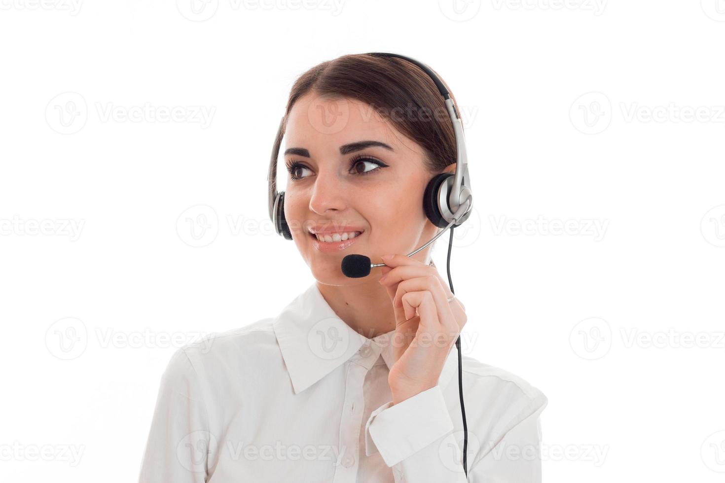 joven y bella mujer morena de negocios con auriculares y micrófono sonriendo y mirando hacia otro lado aislada de fondo blanco foto