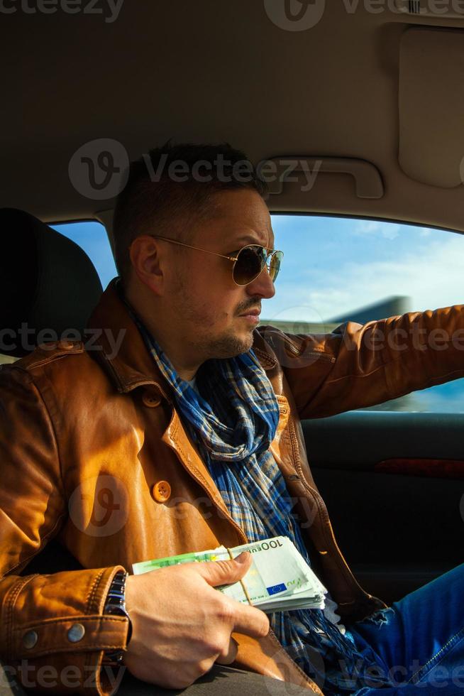 concentrated man in sunglasses with bundle of money in hands driven car photo